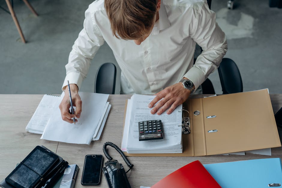 Man in an office reviewing financial papers with a calculator on a desk.